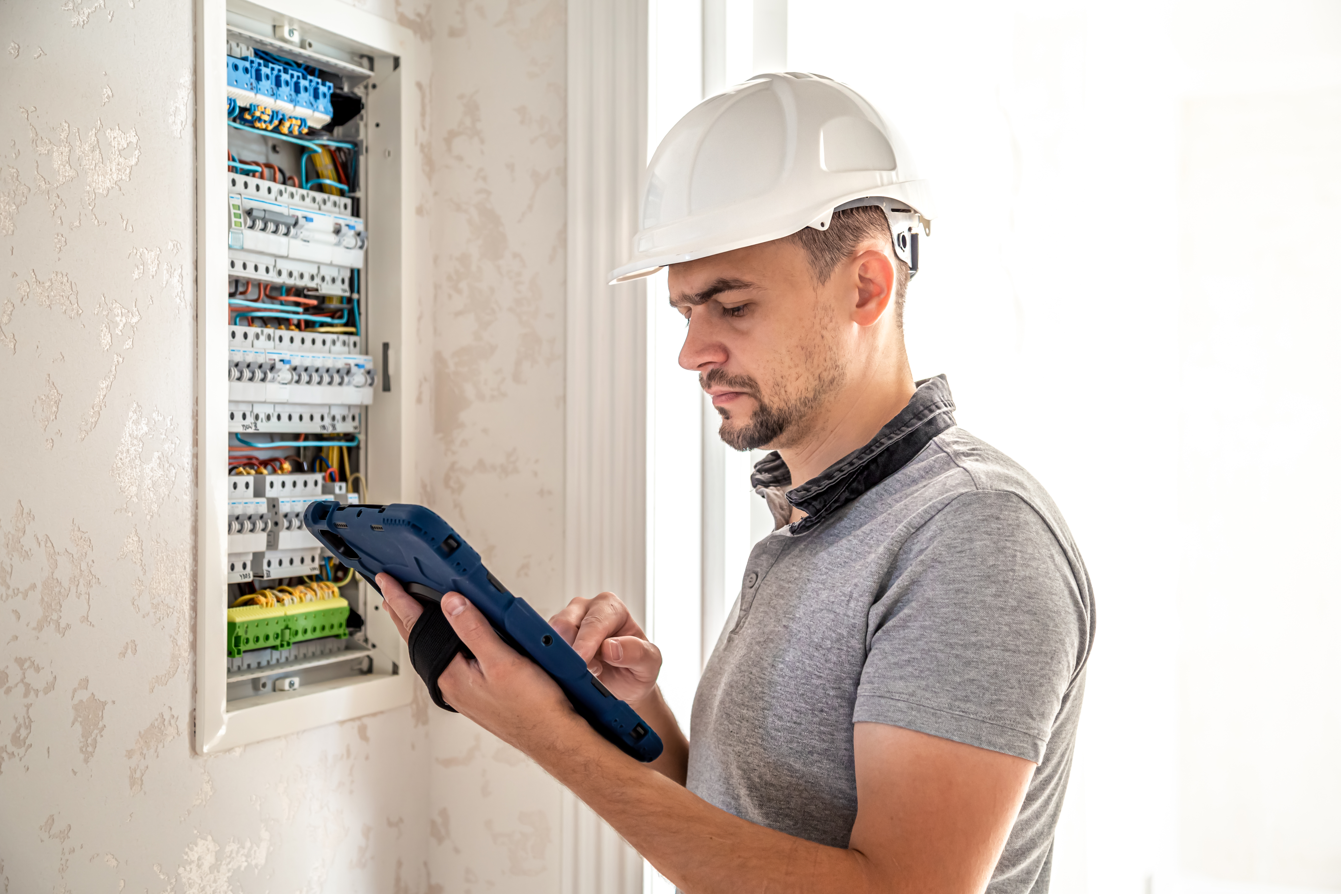 Man, an electrical technician working in a switchboard with fuses. Installation and connection of electrical equipment. Professional uses a tablet.